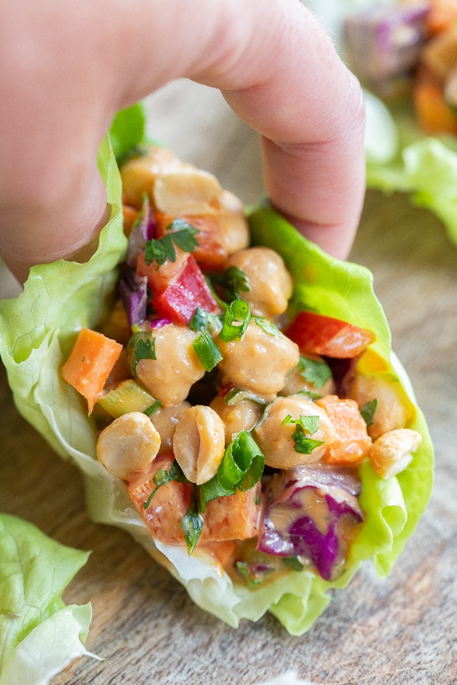 close up of a hand holding a chickpea lettuce wrap with peanut sauce