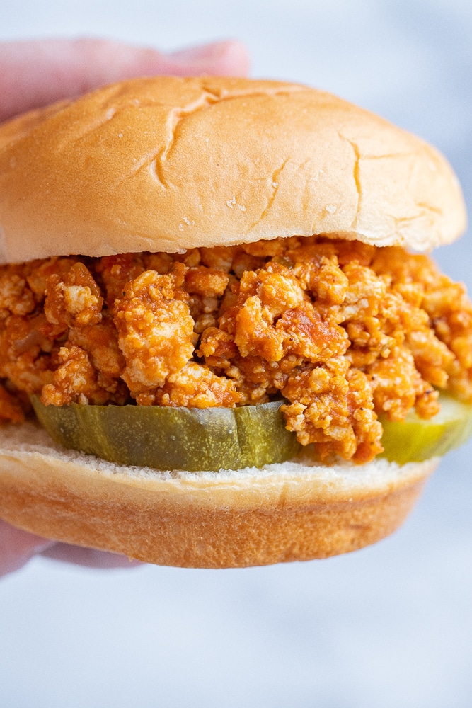 close up of a hand holding a pumpkin sloppy joe with pickles