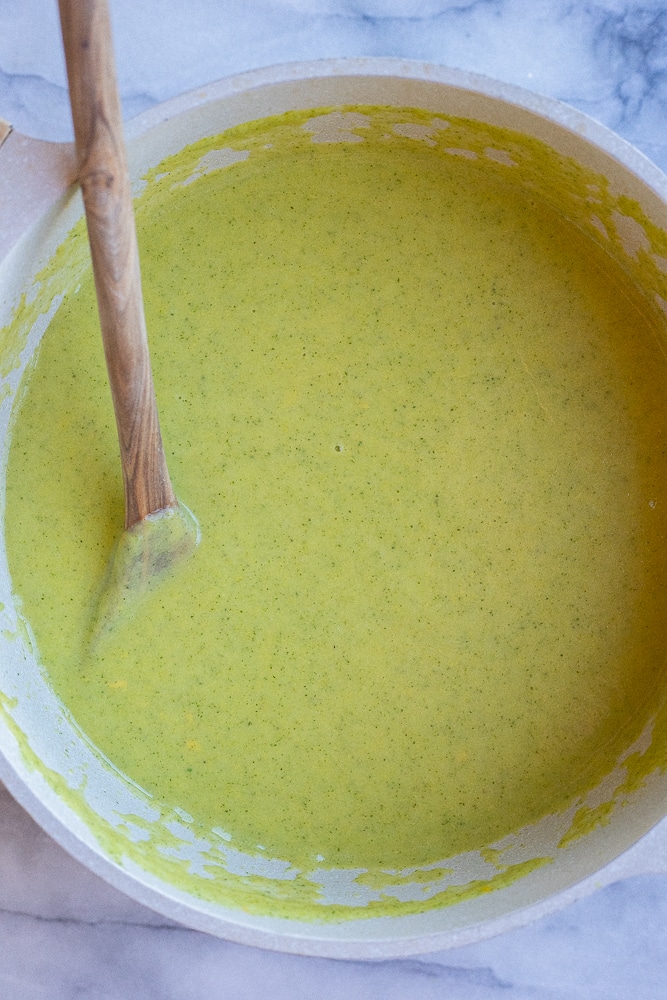 cheesy zucchini soup in a pot with a wooden spoon