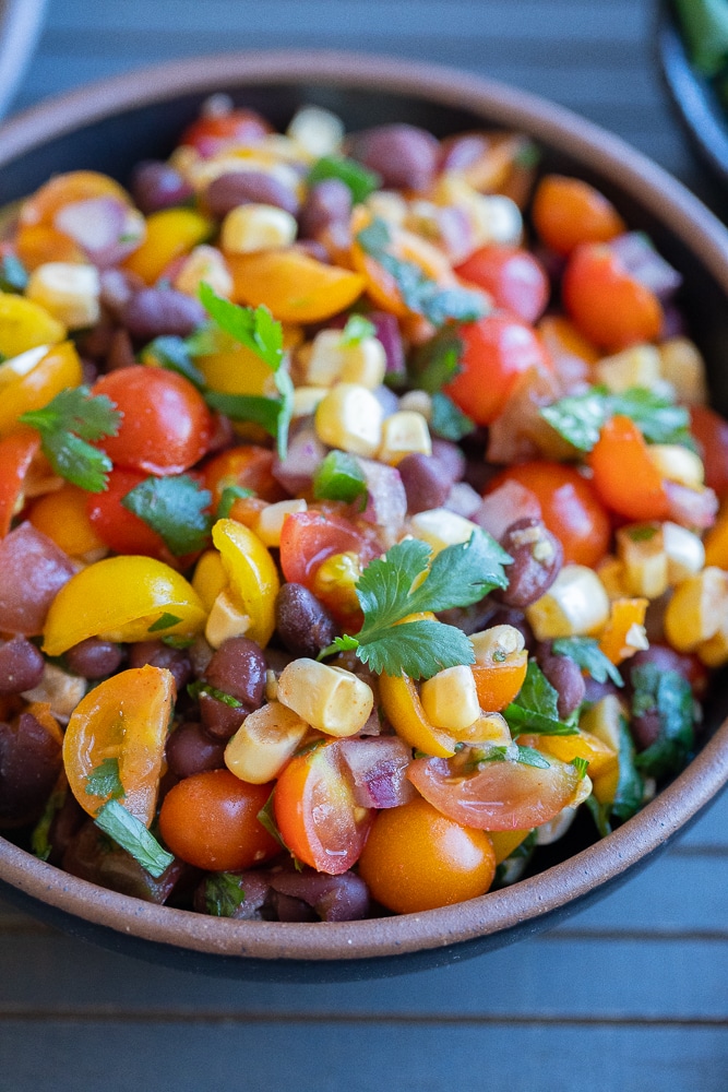 close up of a bowl of cherry tomato, bean and corn salsa with cilantro