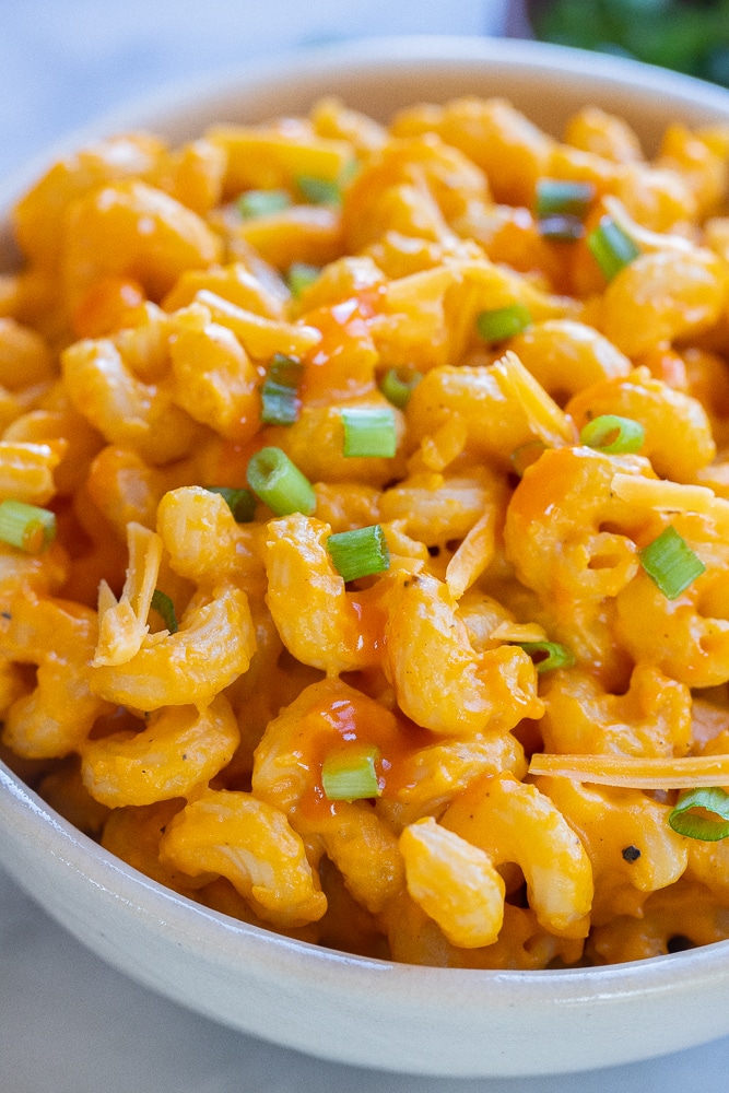 close up of a bowl of cheesy buffalo butternut squash pasta topped with scallions