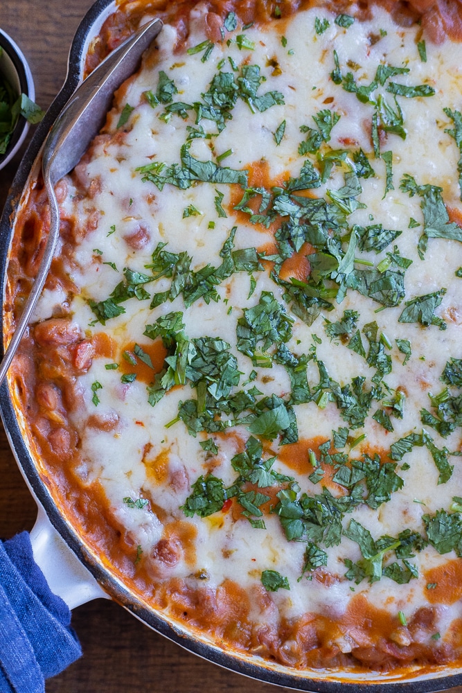 close up of a pan of cheesy pinto beans with green chile topped with chopped cilantro