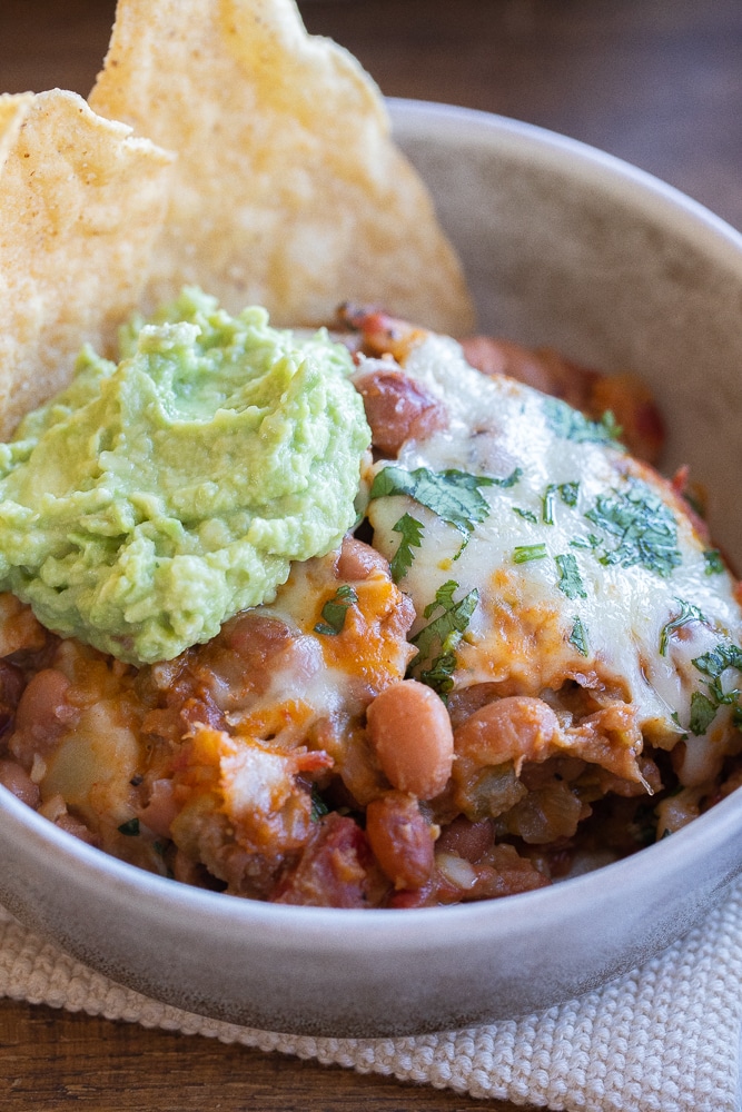 close up of a bowl of cheesy pinto beans with guacamole