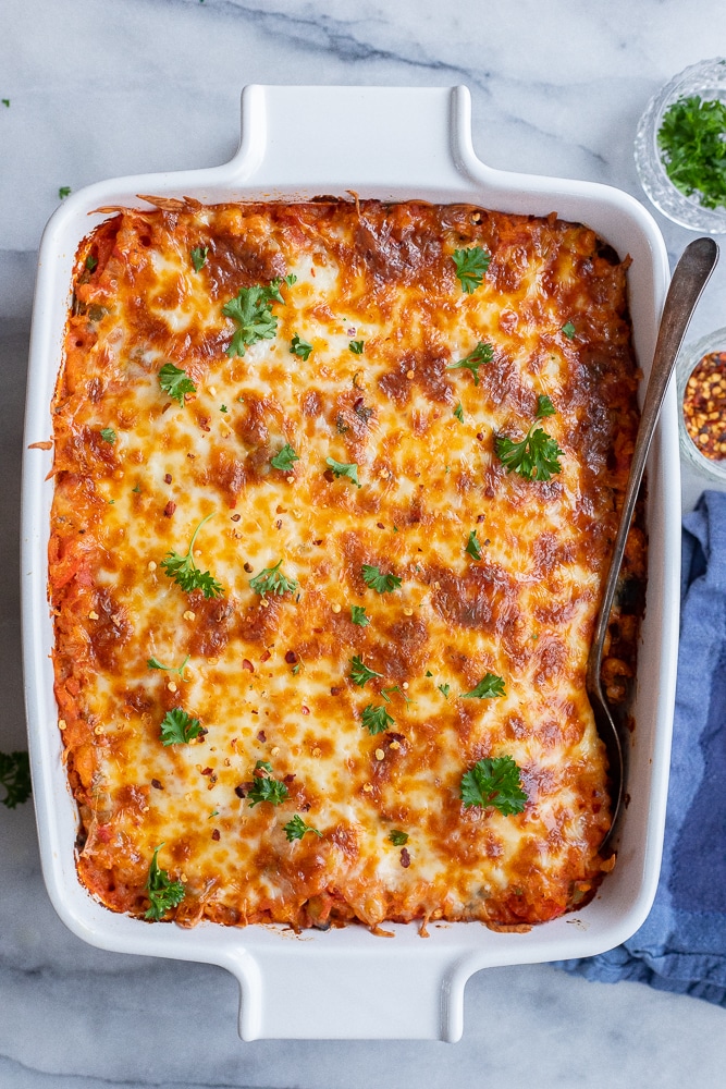 pizza casserole with white beans and rice in a ceramic baking dish topped with fresh herbs