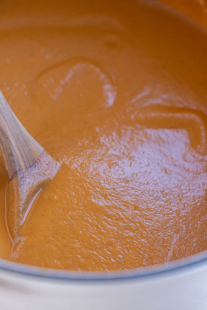 close up of this creamy roasted vegetable soup in a pot with a wooden spoon