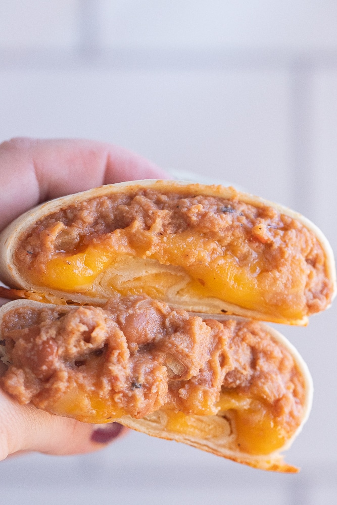 close up of a hand holding a bean and cheese burrito that has been cut in half