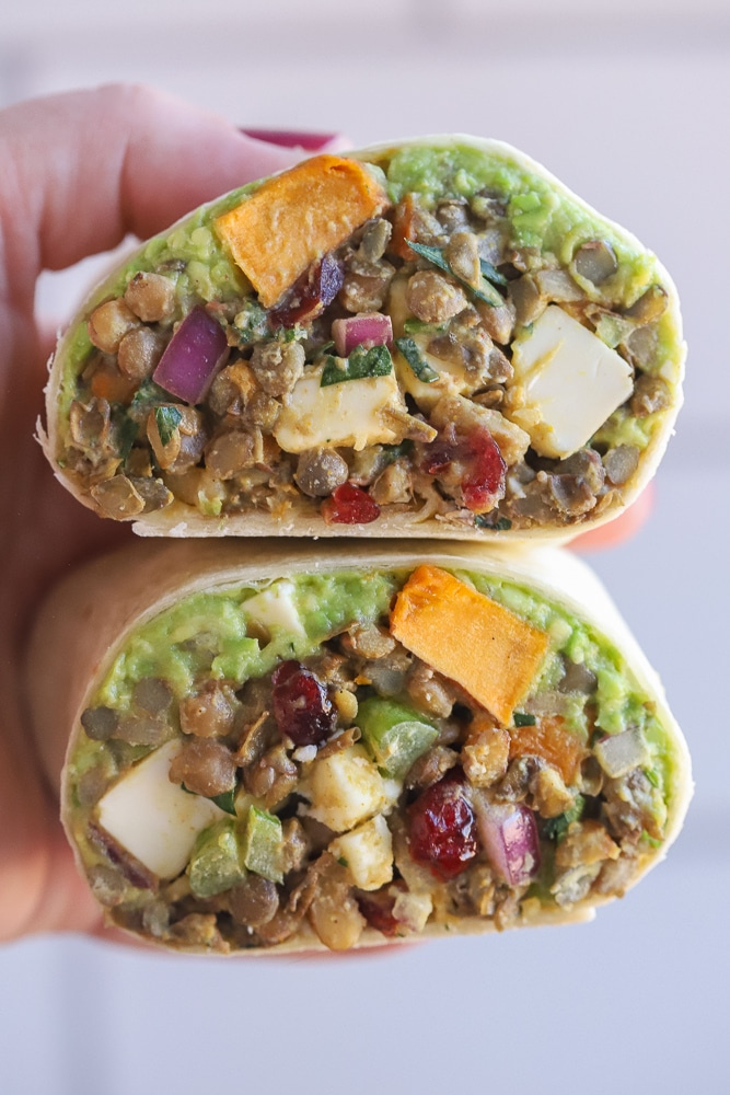 close up of a hand holding a curry lentil wrap with roasted sweet potato and avocado