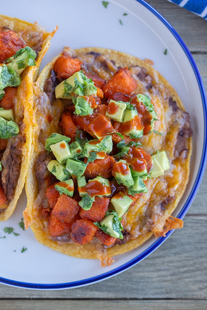 close up of seasoned sweet potato tacos with beans and cheese on a plate