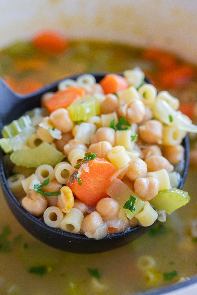 a black ladle holding a big spoonful of this chickpea noodle soup